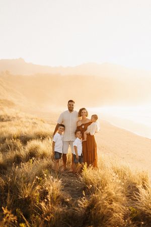 A family stands together on a hilltop during golden hour surrounded by wild grasses.