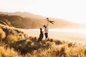 Silhouetted figures play joyfully on a scenic hillside overlooking a golden sunset beach.