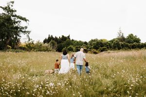 Family walking together through a sunny meadow filled with white wildflowers.