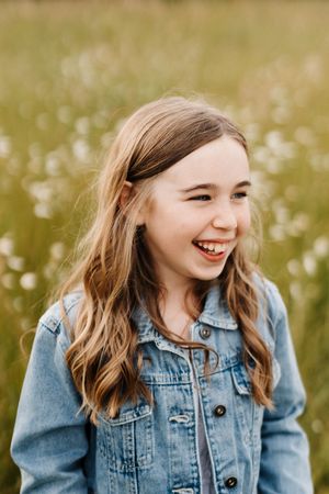 Young person in denim jacket smiling in sunny meadow with white flowers.