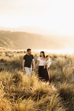 Family walking through golden grass at sunset in a coastal landscape.