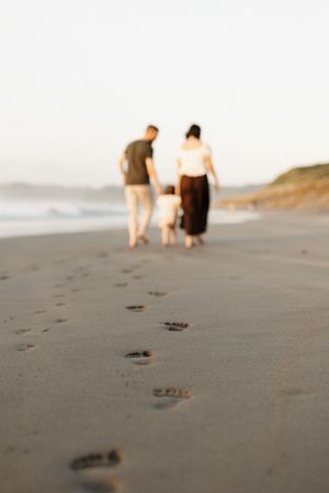 People walking along a beach leaving footprints in the sand during golden hour.