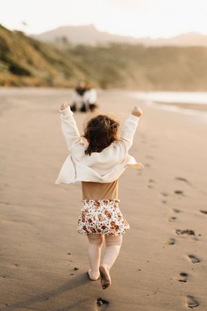 Child in white outfit running on sandy beach at sunset leaving footprints behind.