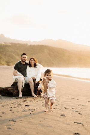 Family enjoying playful moments together on a sandy beach at sunset.