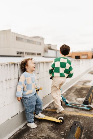 Two children with scooters playing on urban rooftop.