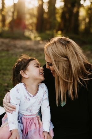 Mother and daughter share a joyful moment together in a sunlit forest setting.
