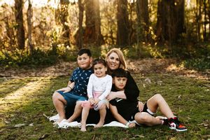 A small group sits together on fallen leaves in a wooded area during golden hour.