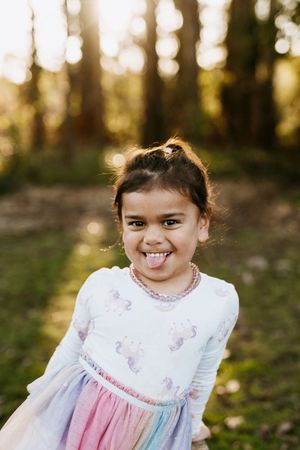 Young person in white and pink dress smiling brightly in forest setting.