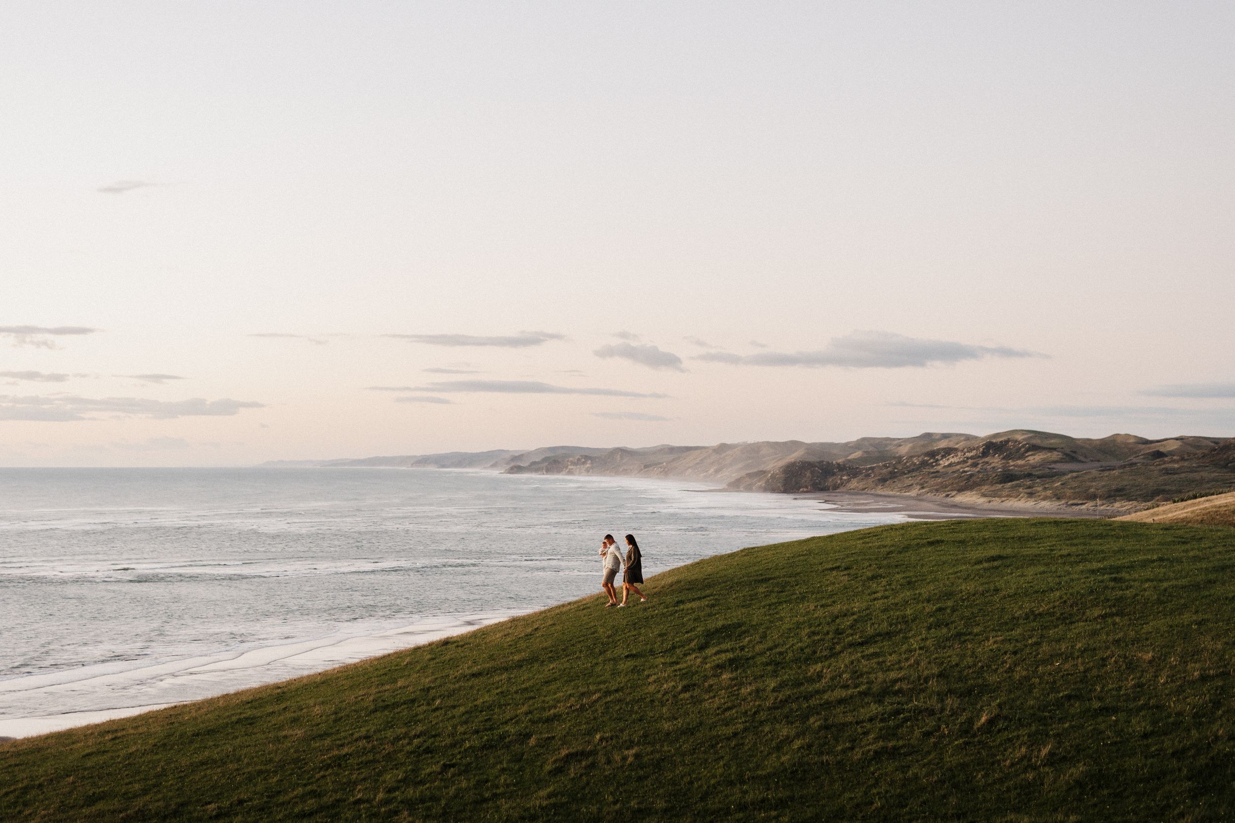 Two people silhouetted against coastal landscape and cloudy sky.