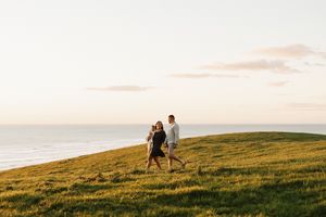 Couple walking together on a scenic coastal hill during golden hour.
