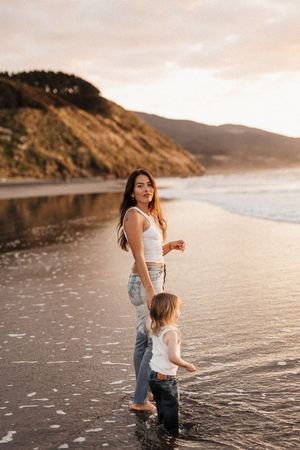 Mother and child exploring beach together near coastal cliffs at sunset.