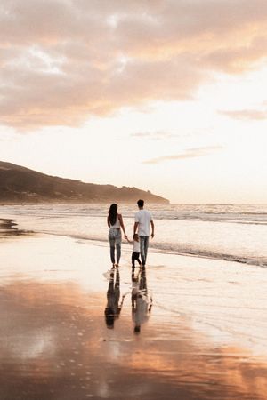 Couple walking hand in hand on wet sand during golden hour at the beach in Raglan, NZ.