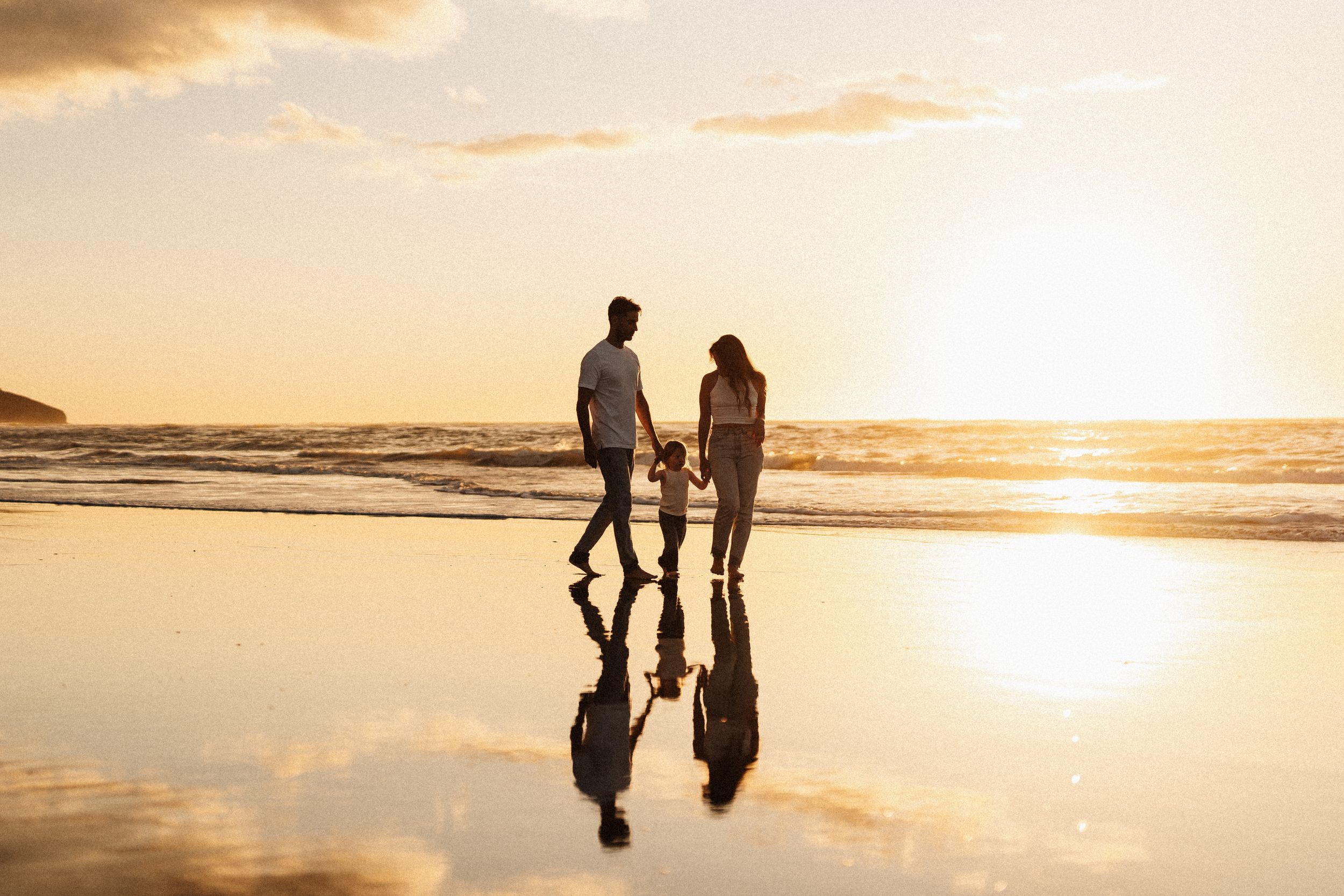 Family walking on a reflective beach at sunset creating mirror-like silhouettes.
