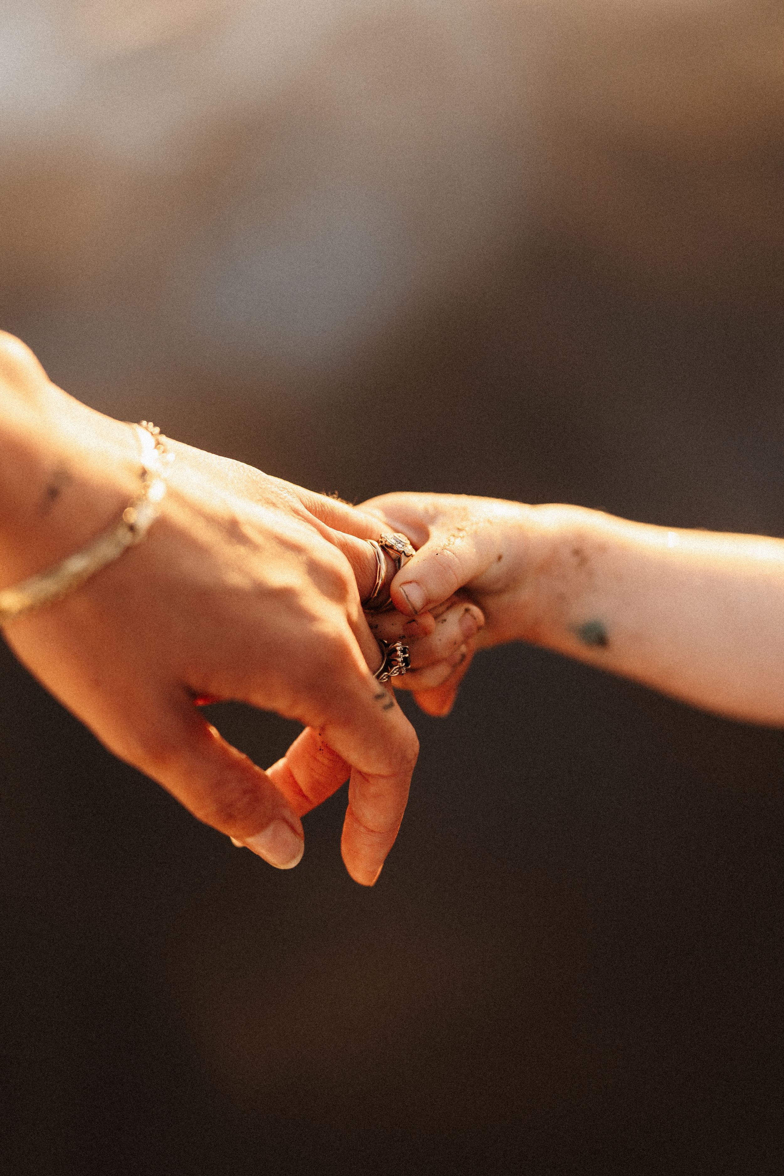 Close-up of two hands with rings gently touching in warm sunlight.