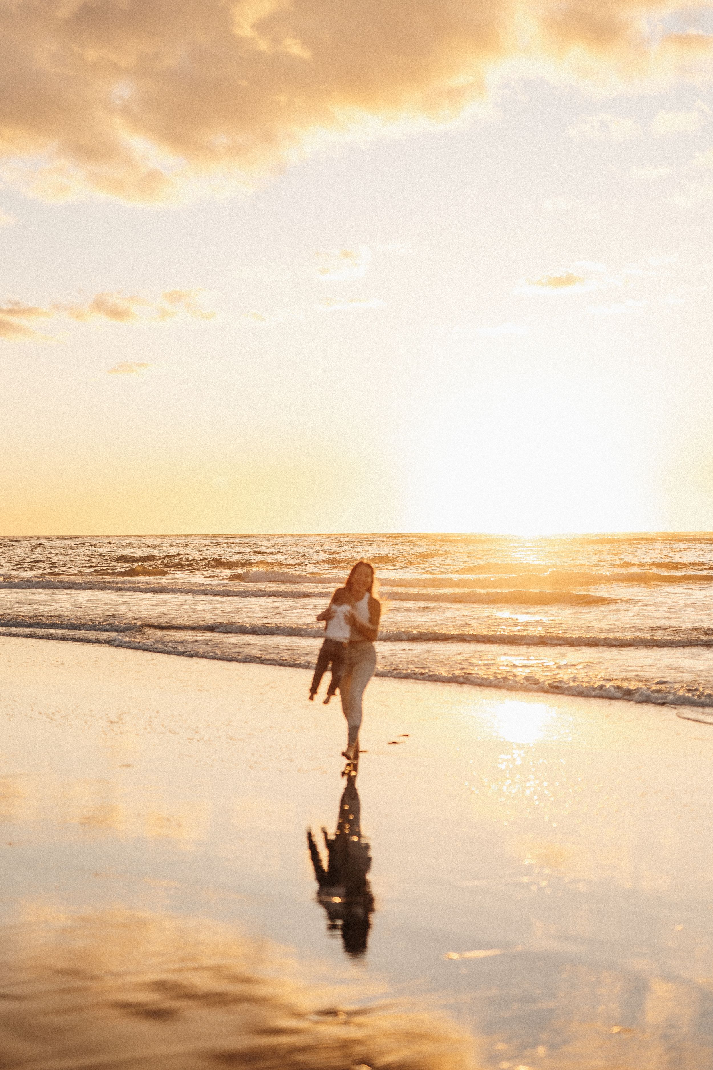 Silhouette of person running on beach at sunset with reflection in wet sand.