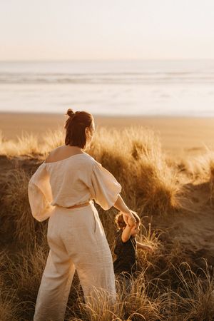 Figure in white clothing walks through golden beach grass at Raglan sunset.