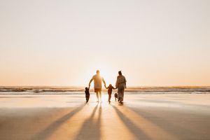 Silhouetted family walking on beach during golden sunset casting long shadows on wet sand.