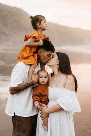 Family of four sharing intimate moment on beach at sunset in coordinated outfits.