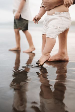 Bare feet splashing in shallow beach water creating reflections on wet sand at sunset.