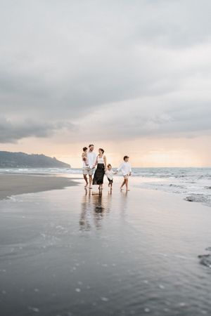 Family walking along misty beach shore at sunset with mountains in background.