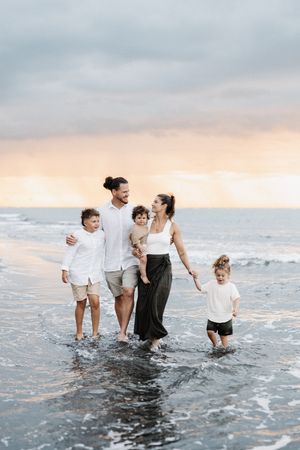 Group wearing white and black outfits playing in ocean waves at dusk.