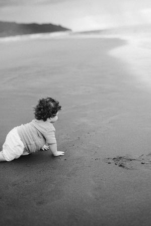 Black and white photo of small child crawling on wet beach sand.