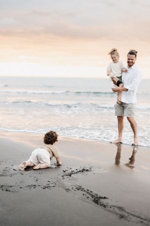 Family playing and drawing in sand on peaceful beach at sunset.