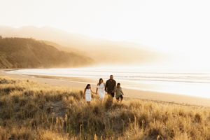 Family walking through golden beach grass at sunset along coastal path.