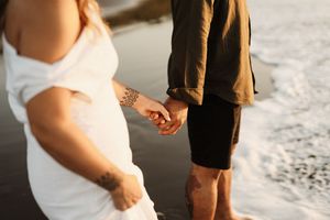 Close up of couple holding hands on beach with cropped view of formal attire.