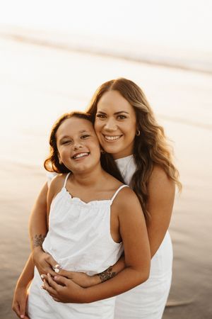 mother and daughter embracing and smiling warmly at sunset on the beach.