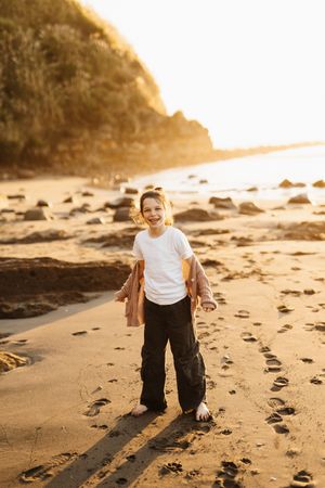 Child smiling and playing on sandy beach during golden hour.
