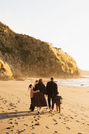 Family walking together on a beach at sunset with cliffs in background.