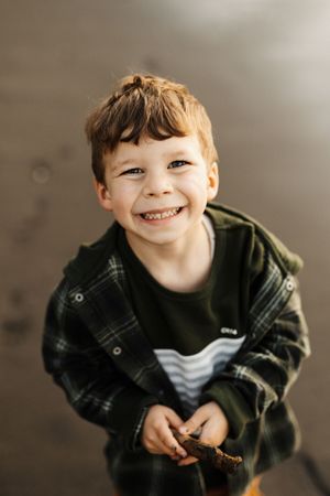 Young boy in plaid jacket smiling brightly at camera.