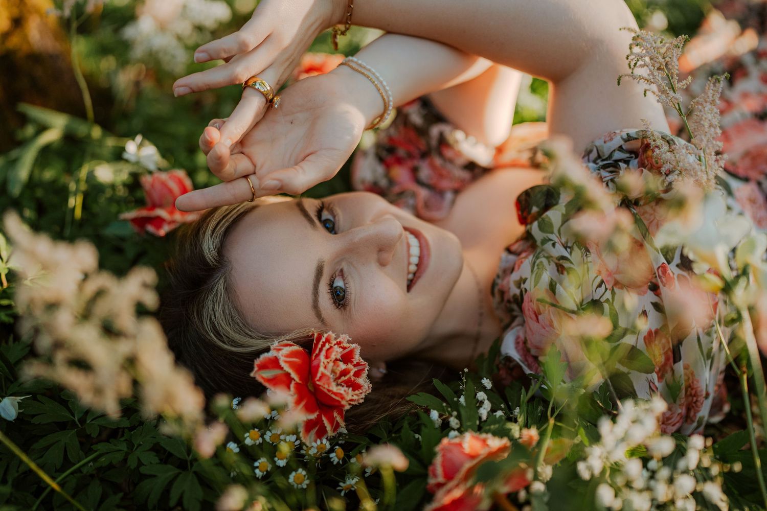 A person lying in a garden surrounded by delicate pink and red flowers in warm sunlit natural lighting.