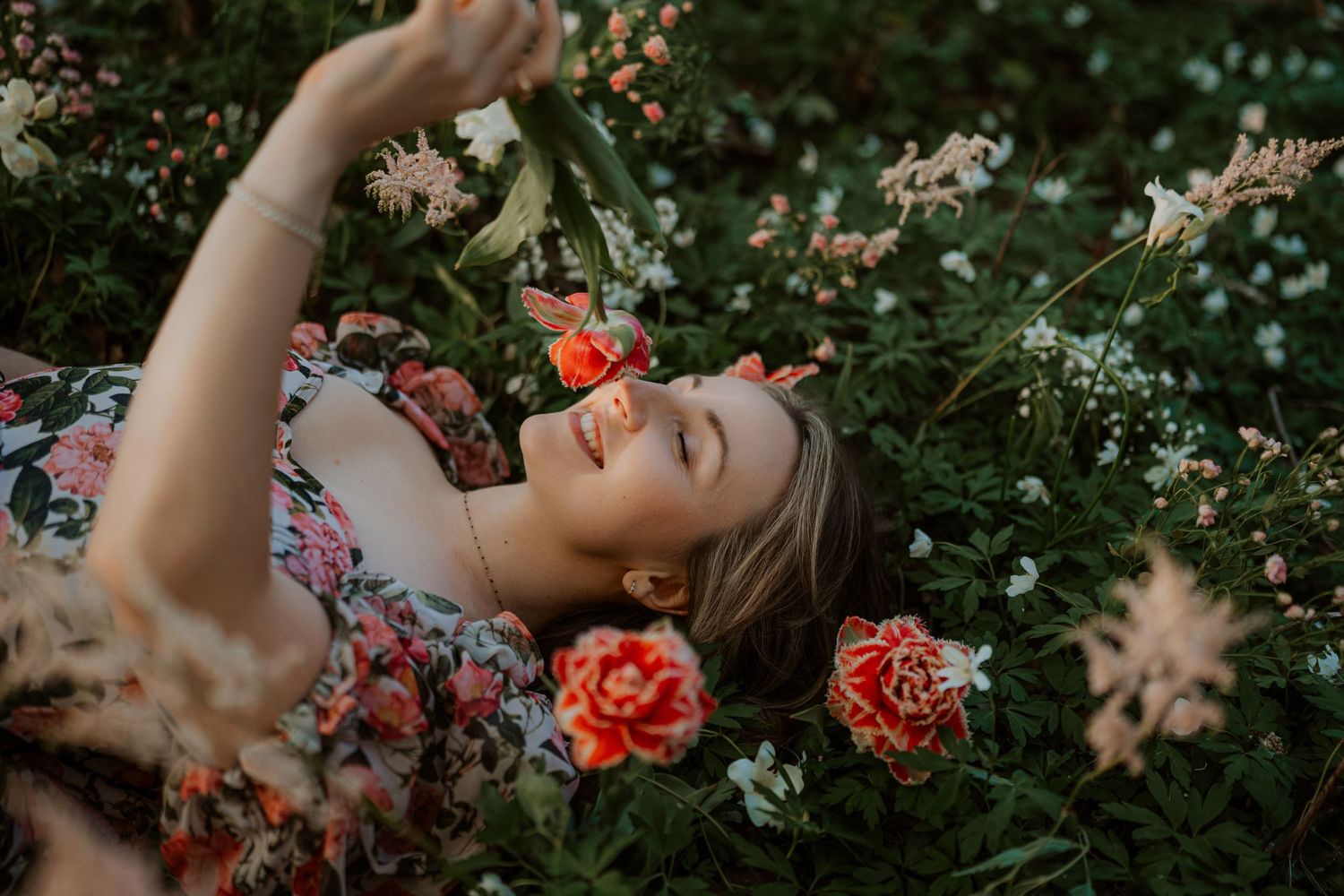 Person lying in garden with pink roses and white wildflowers on sunny summer evening.