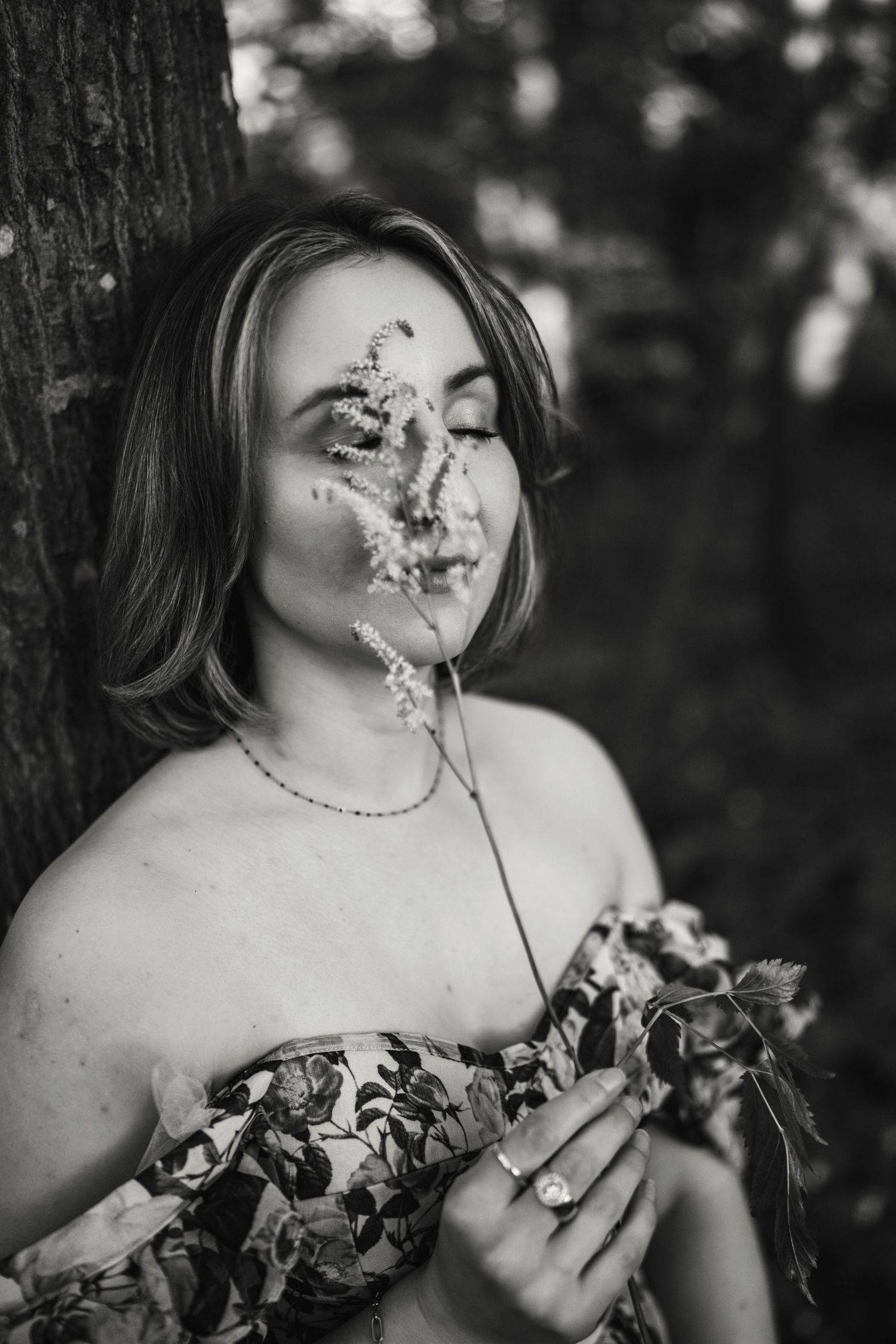 A black and white photo series shows someone holding delicate flowers near their face in an artistic outdoor portrait session.
