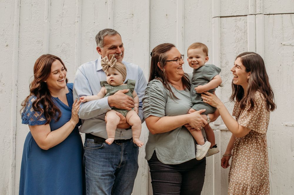 A playful family photoshoot series showing laughter and joy against a white barn wall.