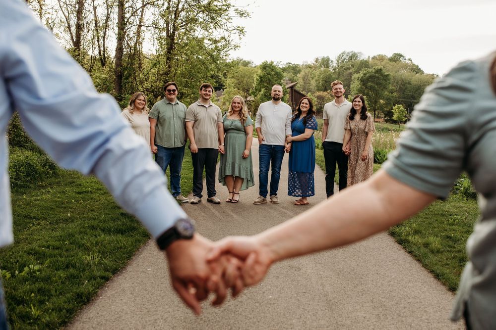 A group photo framed by two people holding hands in the foreground with others standing on a path.