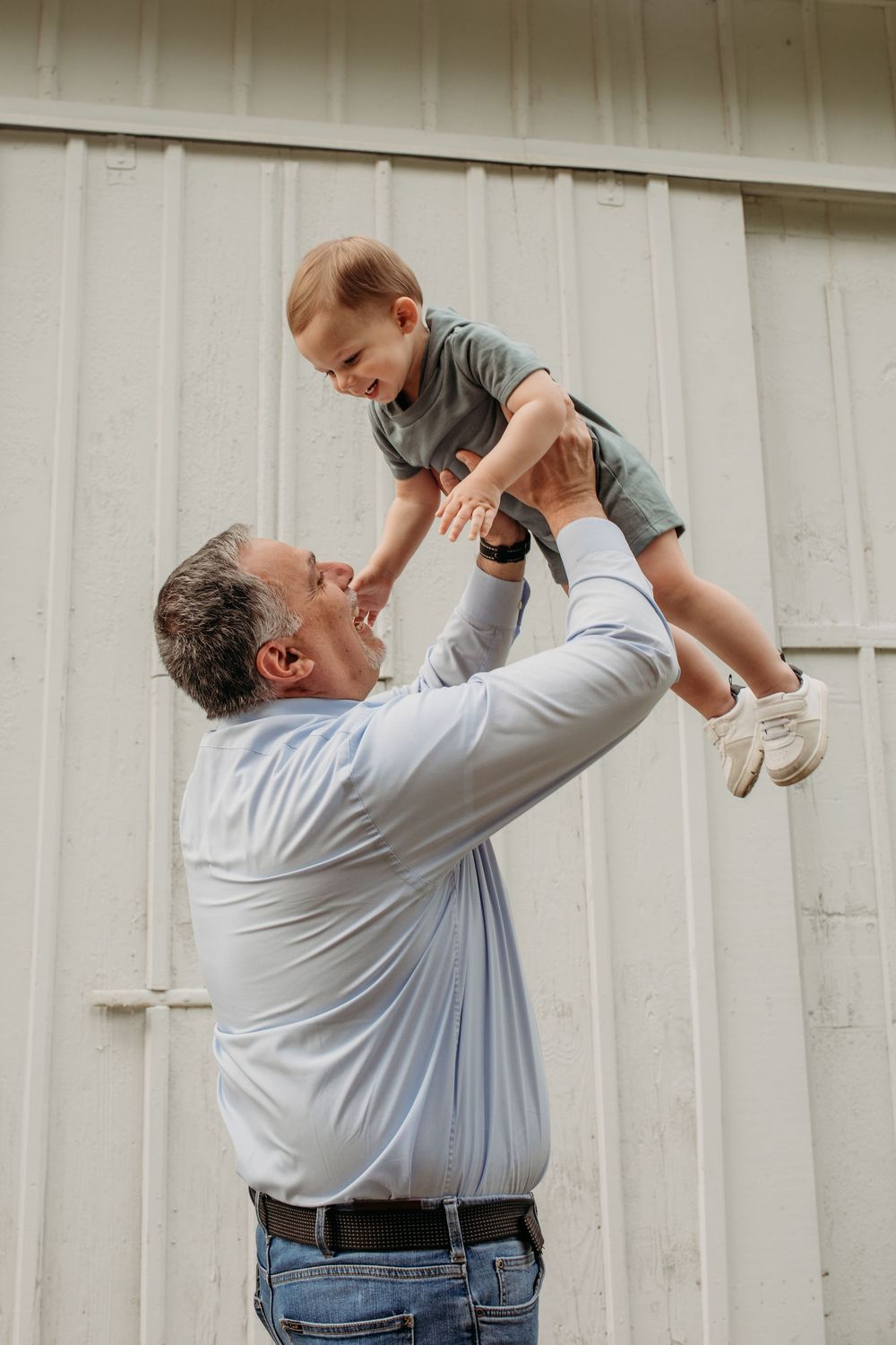 Candid moments of a parent lifting and playing with a small child in front of a white wall.