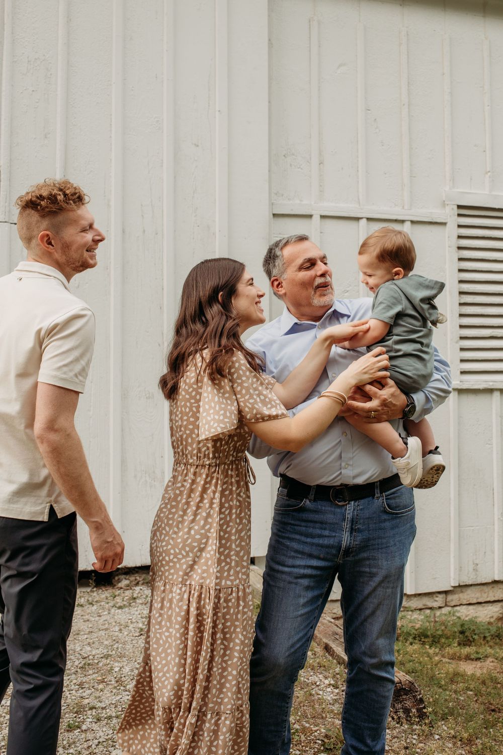 Family members sharing joyful interactions while standing against a white exterior wall.