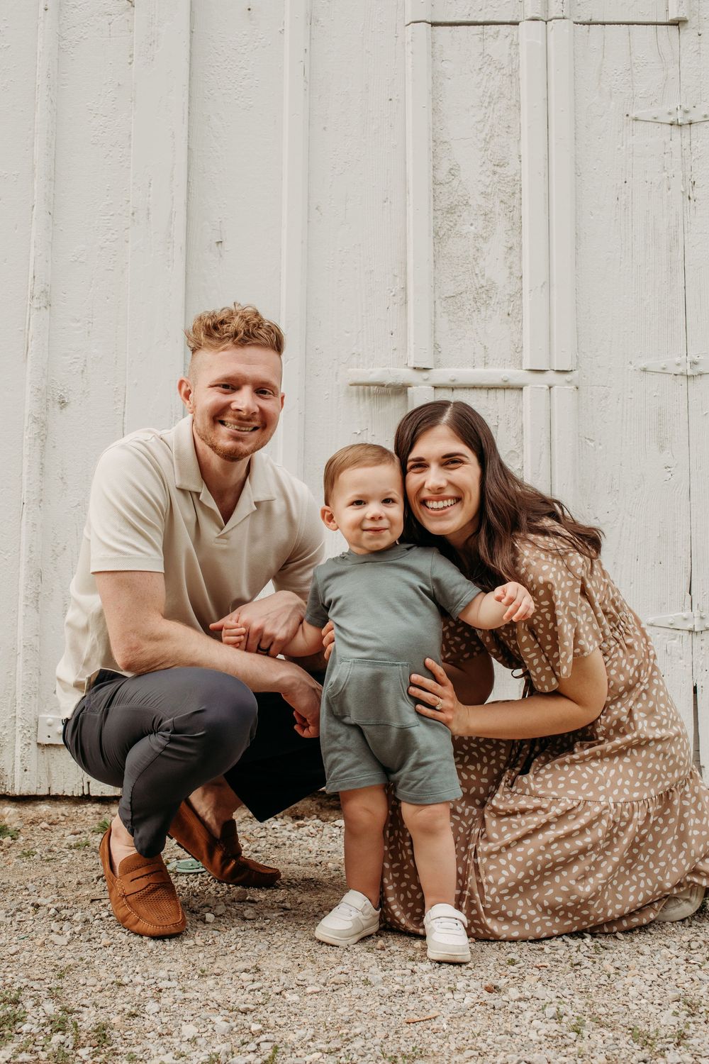 Family members crouching and smiling together on gravel ground next to a white wall.