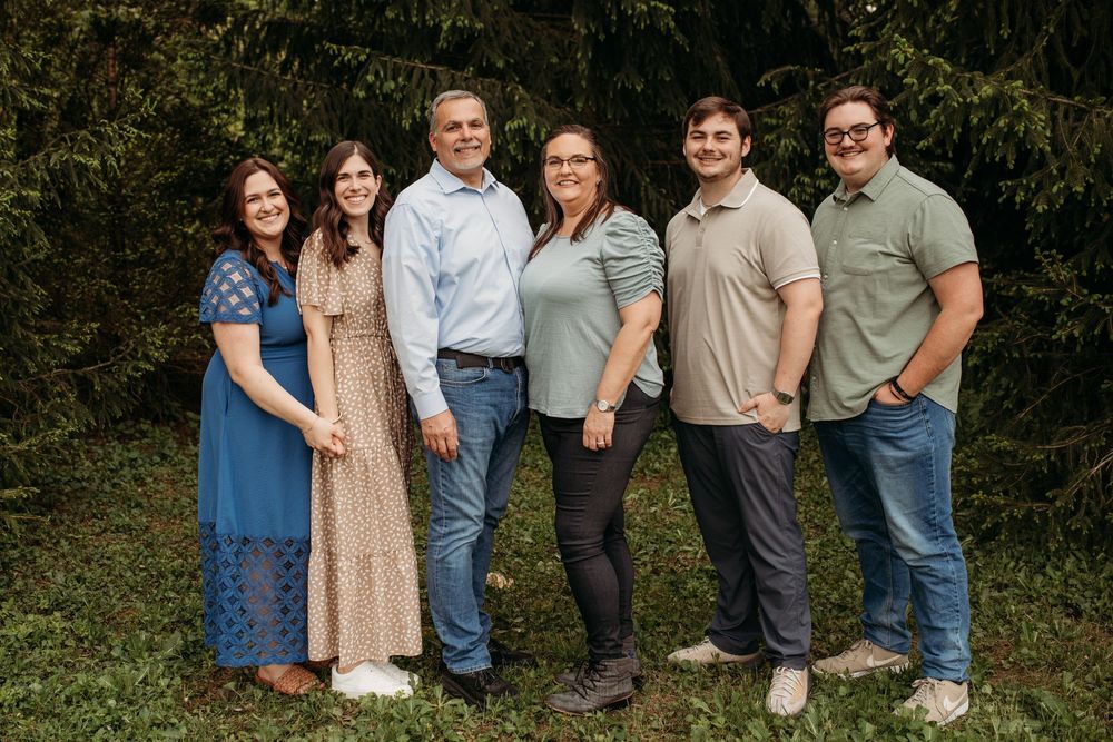 Family group photo session outdoors with people lined up against natural foliage background.