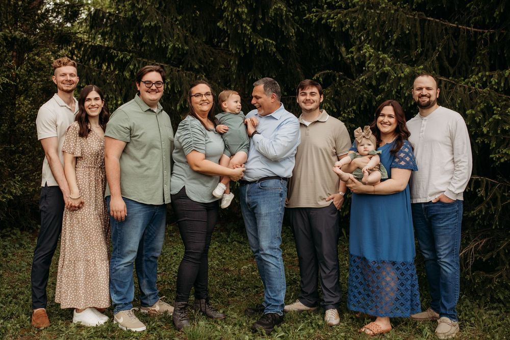 Extended family members pose together for a portrait against a natural backdrop of trees.