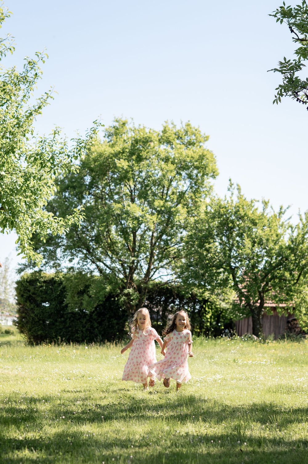 Kleine Kinder in passenden rosa Kleidern spielen auf einer friedlichen grünen Wiese an einem sonnigen Frühlingstag.