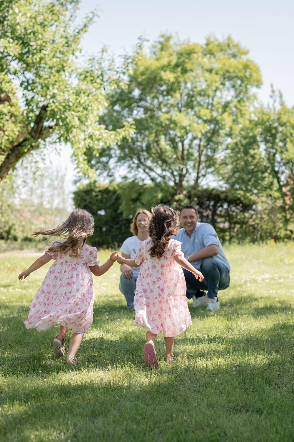 Kinder in passenden rosa Kleidern rennen an einem Frühlingsvormittag fröhlich durch eine sonnige grüne Wiese.
