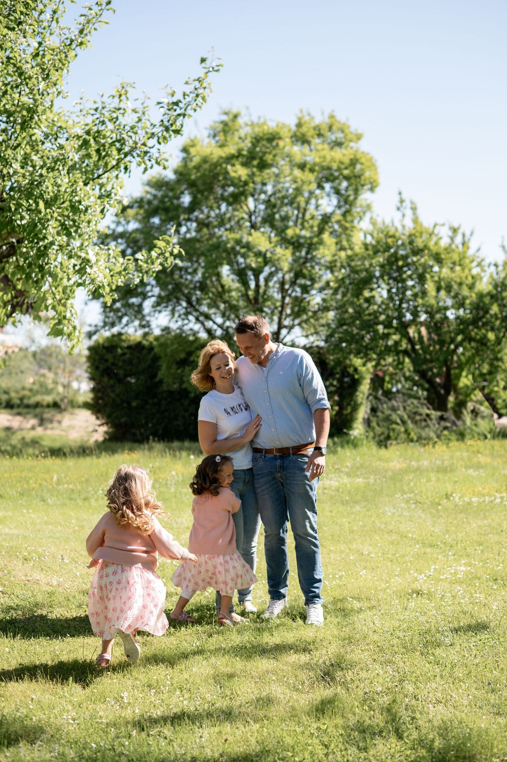 Eine Familie genießt einen sonnigen Frühlingstag in einem üppigen grünen Garten mit Bäumen im Hintergrund.