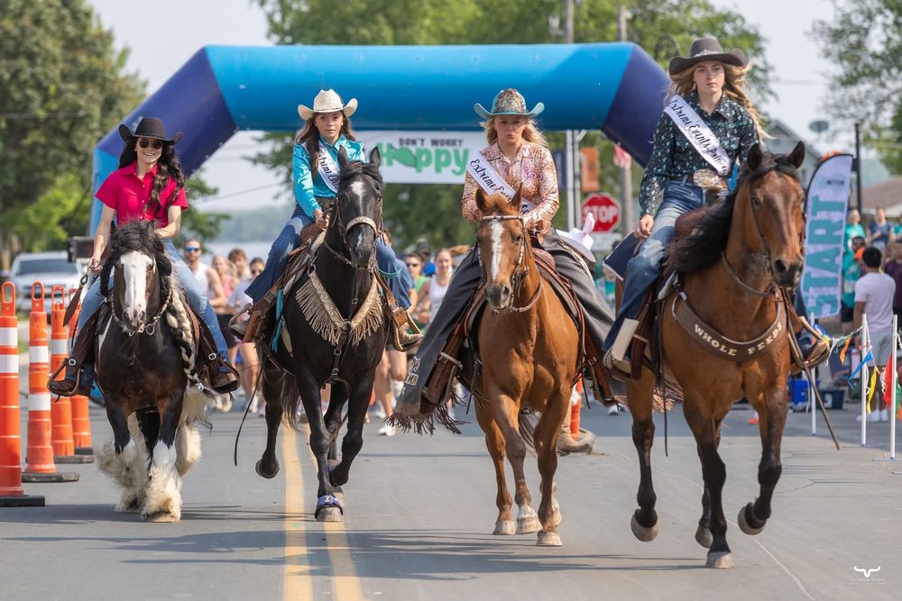 Four horses and riders race down a street under a blue inflatable arch. Pro Rodeo PRCA Rodeo Photographer Dakota Cardenas