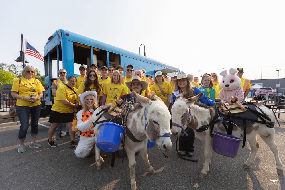 A group gathers around donkeys wearing yellow shirts near a blue bus. Pro Rodeo PRCA Rodeo Photographer Dakota Cardenas