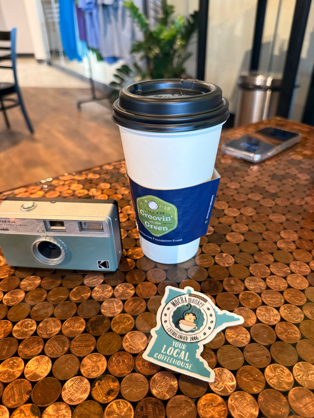 Coffee cup and vintage camera on a penny-covered table surface at a cafe.