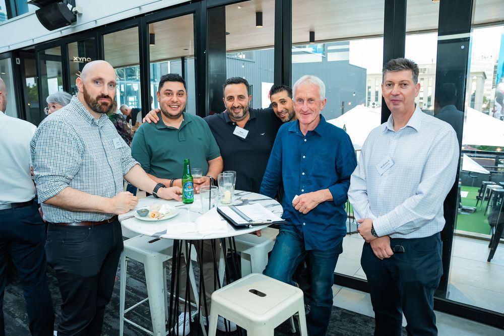 A group of professionals gathered in a modern office space for a business meeting around conference tables.